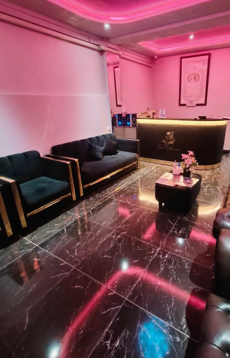 Reception desk and lounge with dark sofas, a marble floor and soft pink lighting